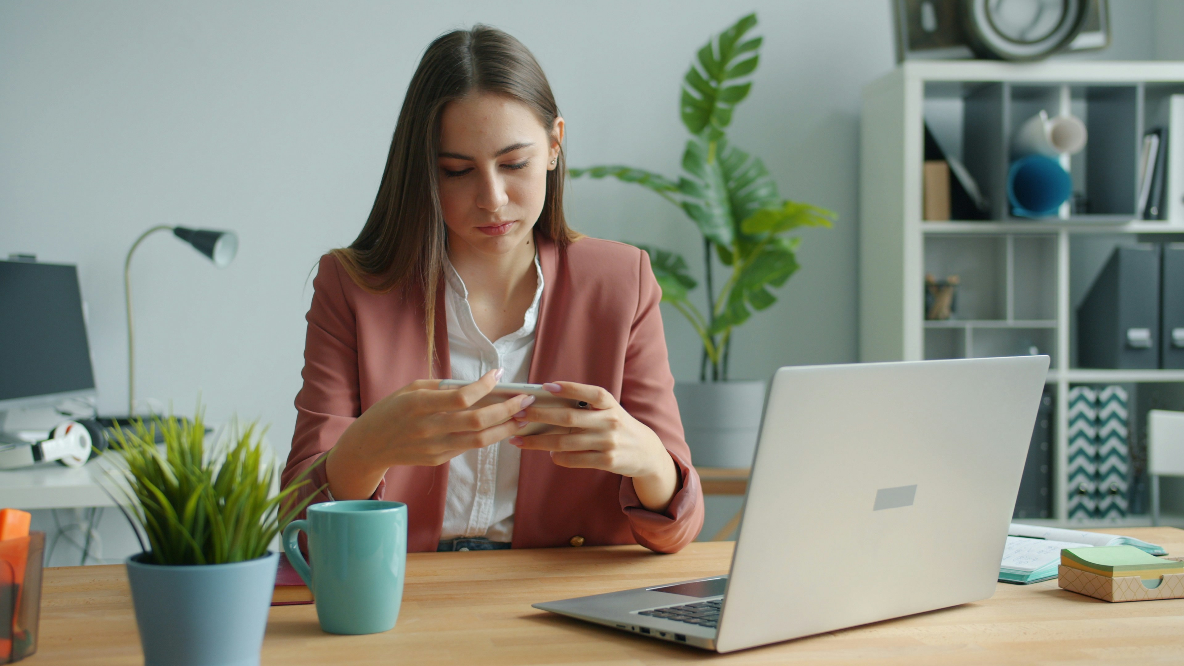 Employee at an office desk examining a suspicious email on her phone next to a laptop